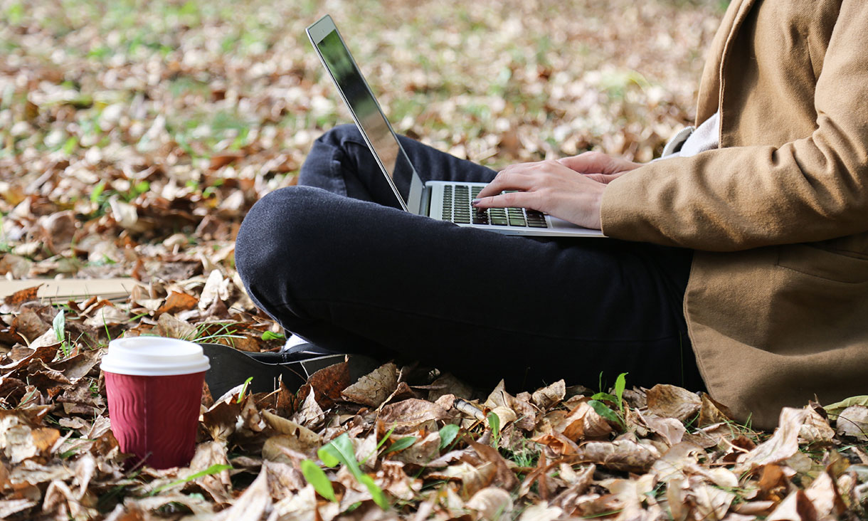 Young woman sitting in park with laptop and coffee.