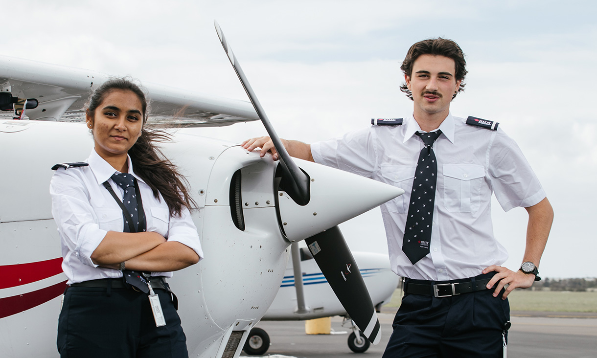 female and male Association Degree in Aviation (Professional Pilots) students standing in front of a plane with arms crossed.