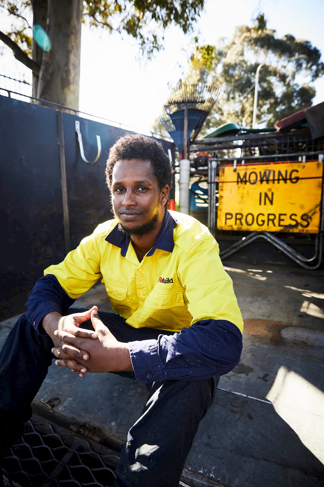 A man sitting alongside fencing and signs in work clothing.