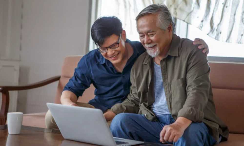 Young person with their arms around elderly person both looking at laptop