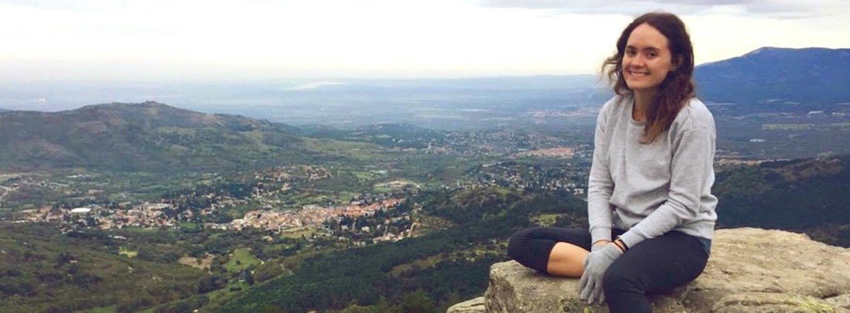 A student sits on a rock with a mountain view in the background.