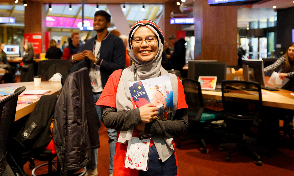 A student holding RMIT brochures smiles at the camera.