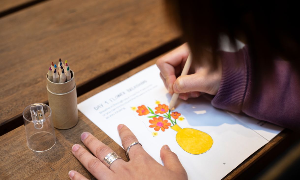 A student colours in a drawing of flowers in a vase.
