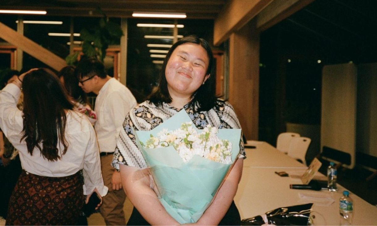 Student standing smiling holding flowers 