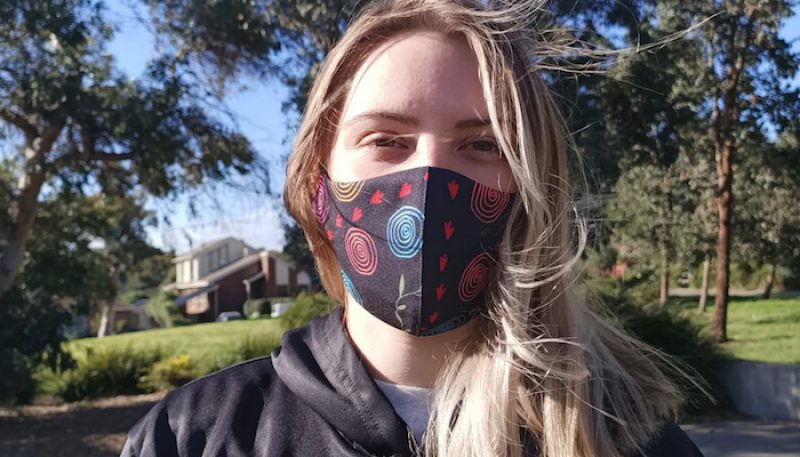 A student stands in nature, wearing a mask.
