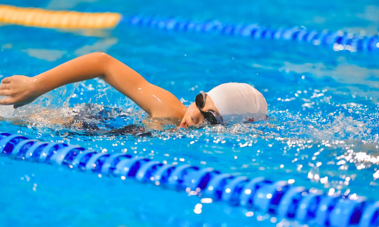 A person swimming freestyle, wearing goggle and a swim cap.