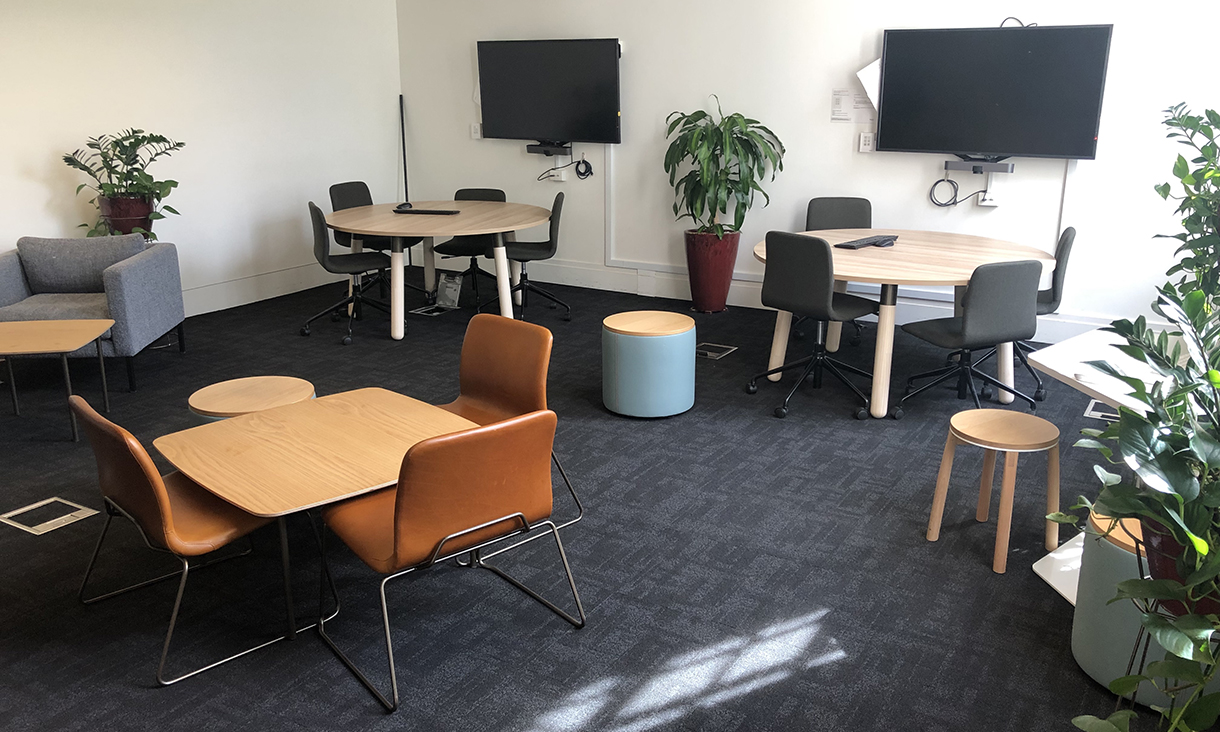 Interior photo of the MBA Edge collaborative learning centre featuring tables and chairs, arm chairs, pot plants and and wall mounted TV screens.
