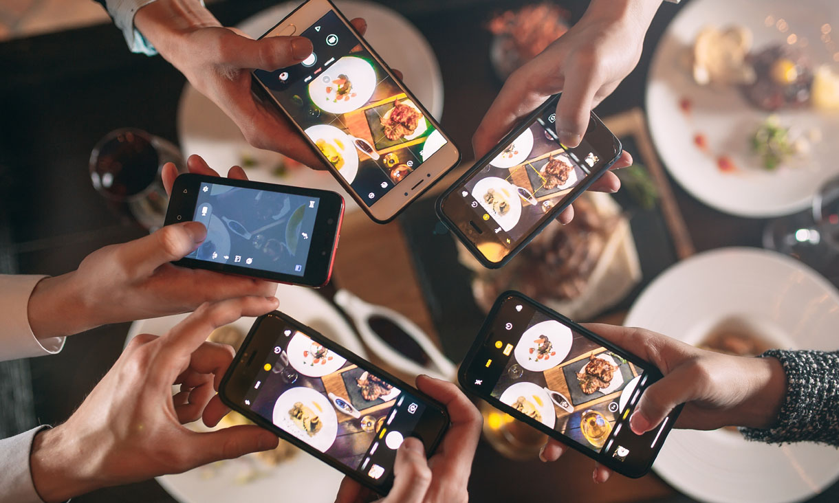 A bunch of people at a dinner party taking photos of their food using their smartphones.