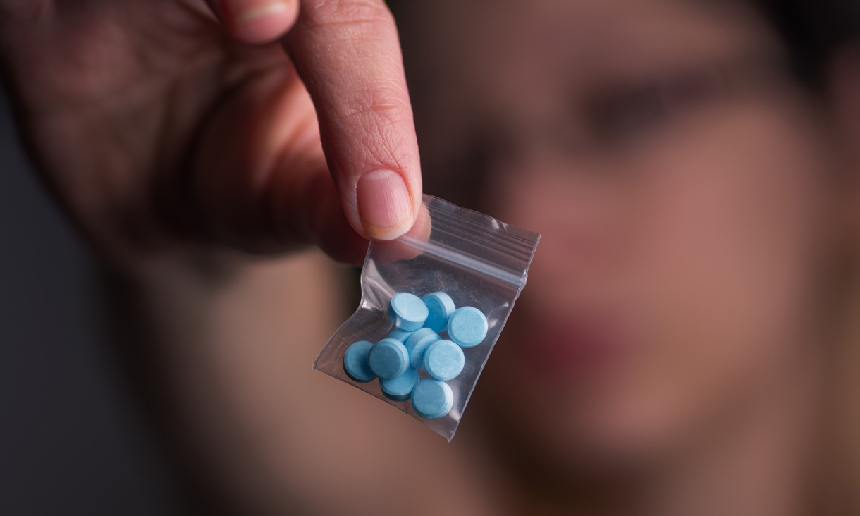 A person holding a tiny ziplock back with several blue pills in it.