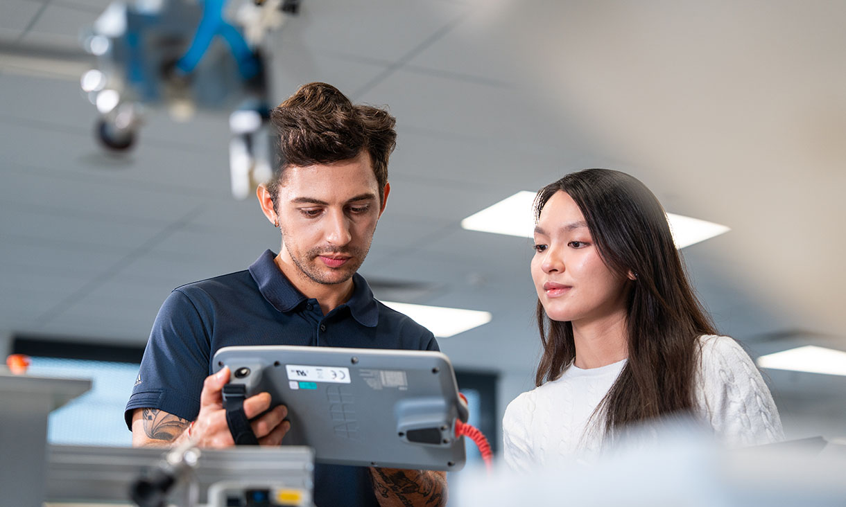 Two people in a lab using a digital tablet to operate or inspect equipment.