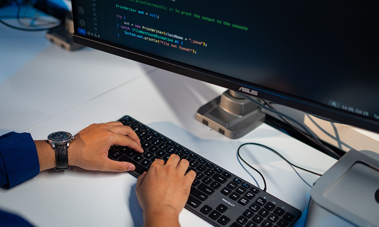Person typing at a desktop computer with code displayed on the monitor, representing programming or software development.