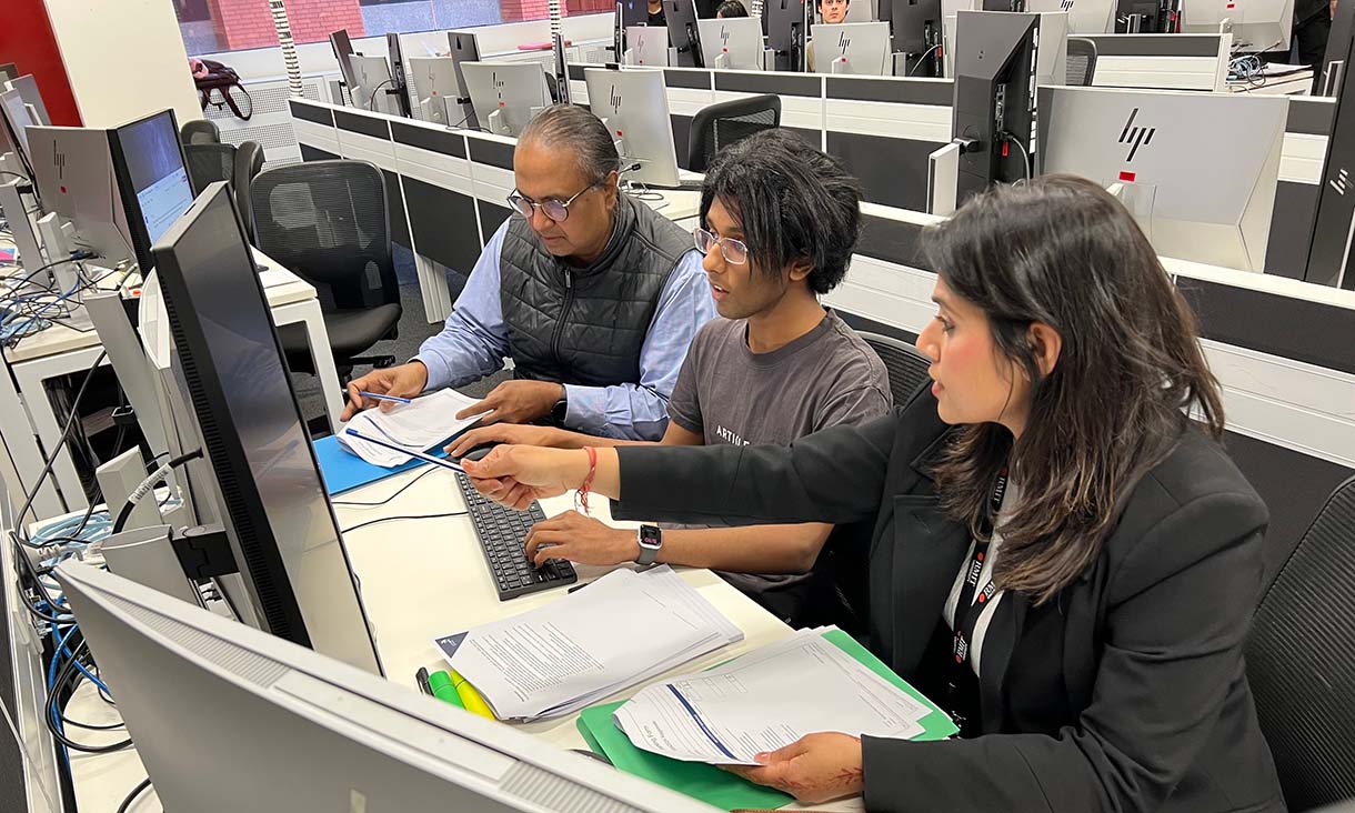 Three people are sitting at a computer together and in the middle of a discussion.