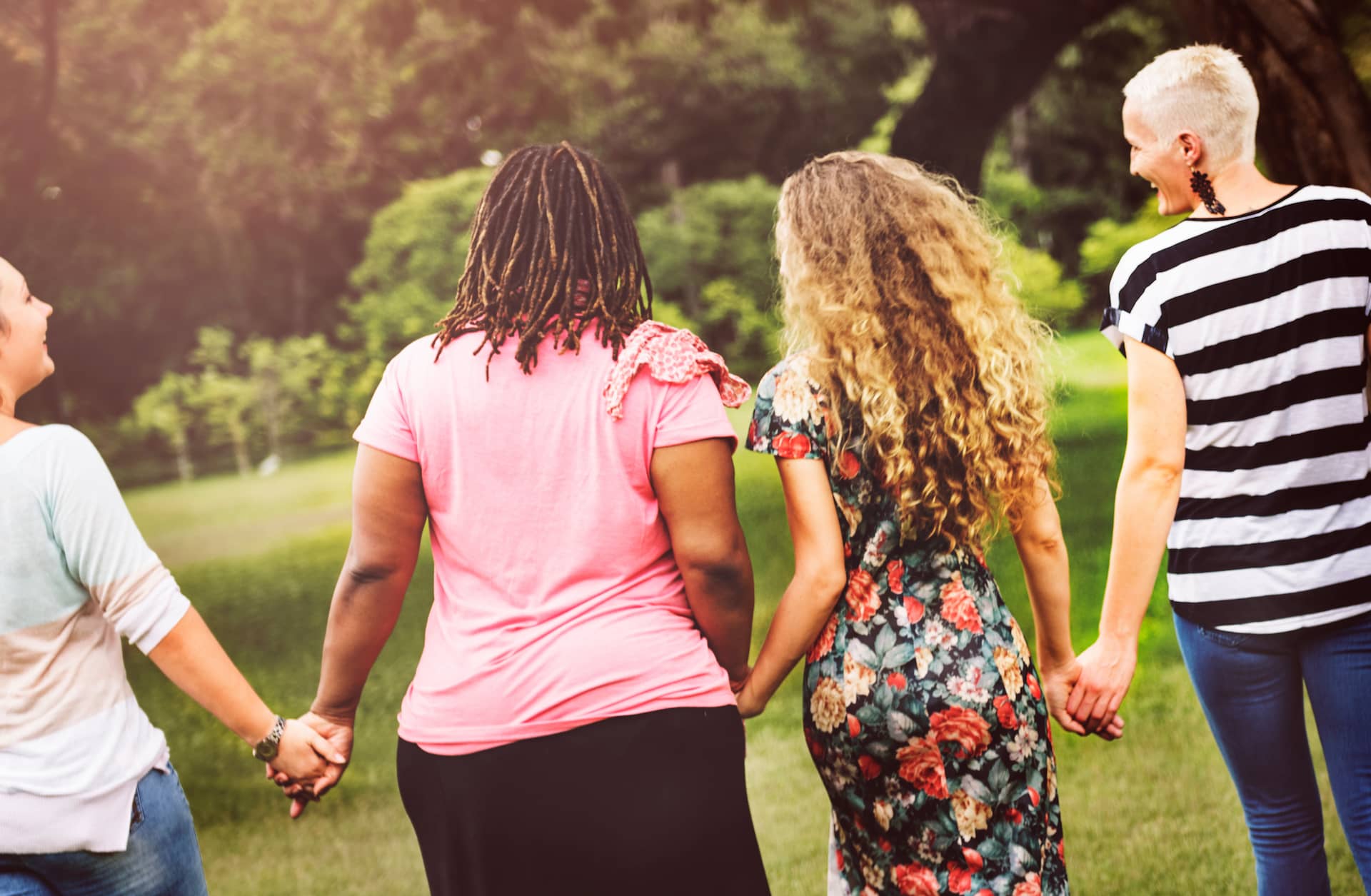 Back view of four people holding hands in park