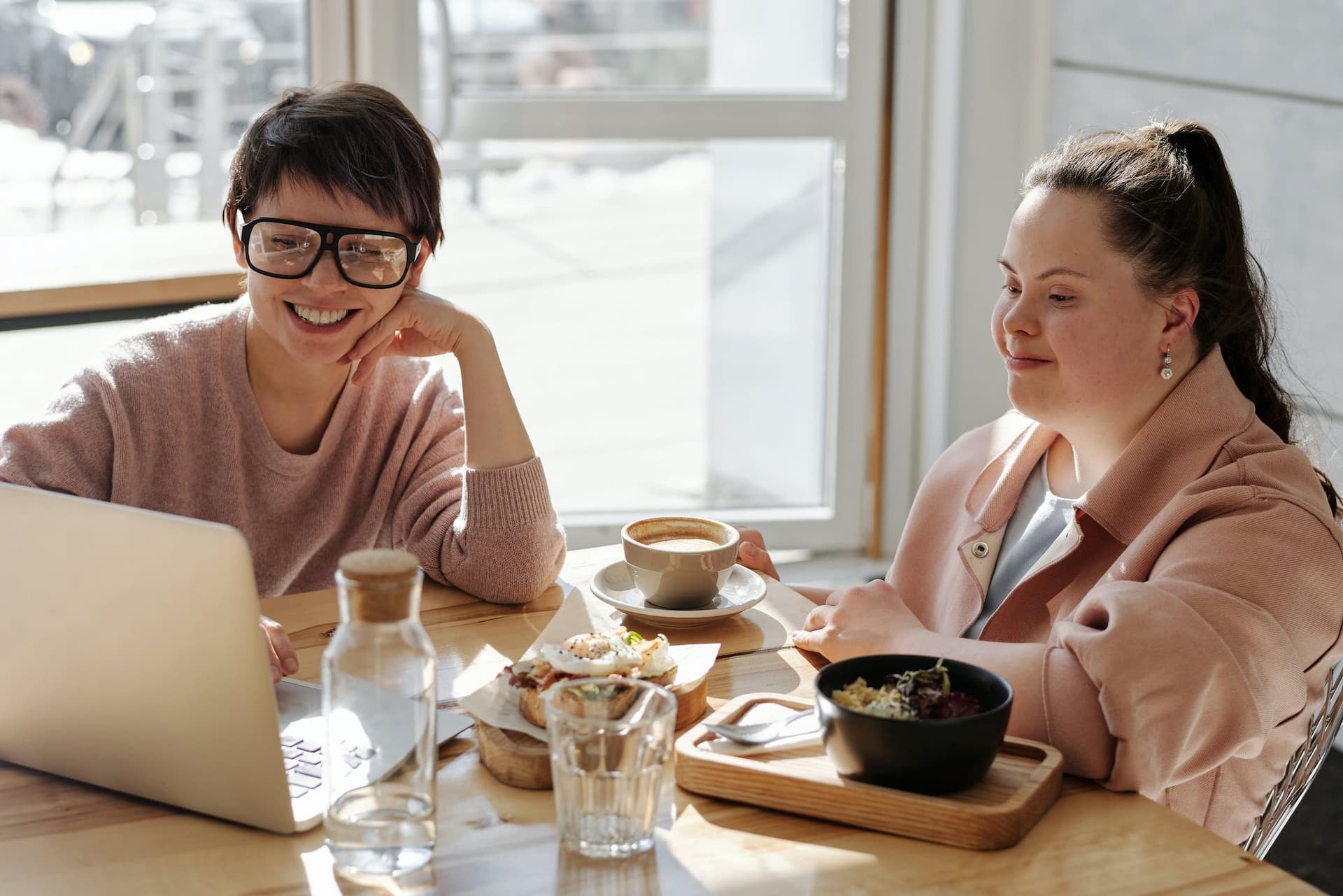 Two people meeting over lunch and coffee looking at a laptop