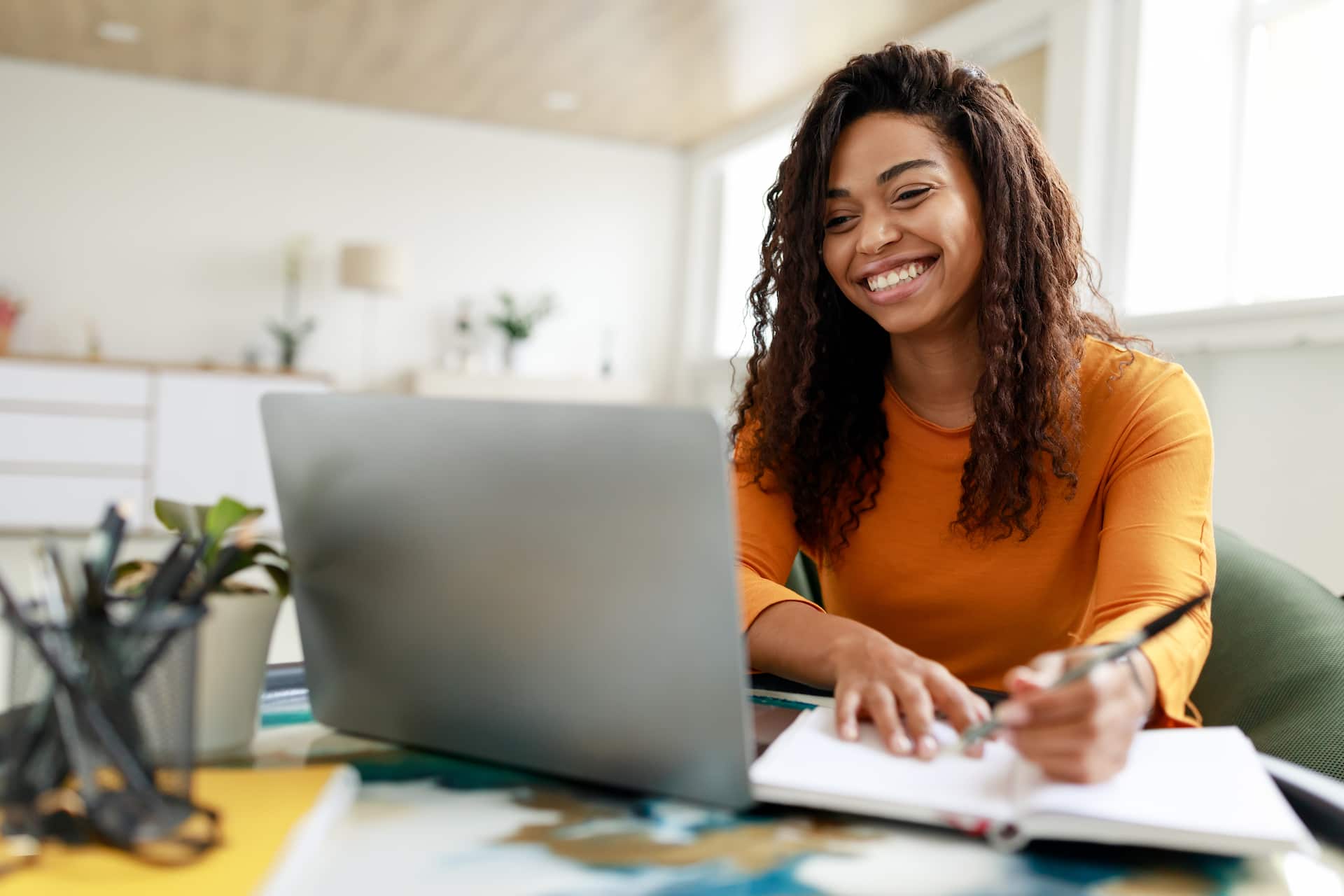 Person smiling and taking notes looking at a laptop