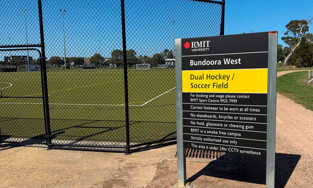 A fenced dual hockey and soccer field at Bundoora West campus, with an RMIT signboard describing the facility.