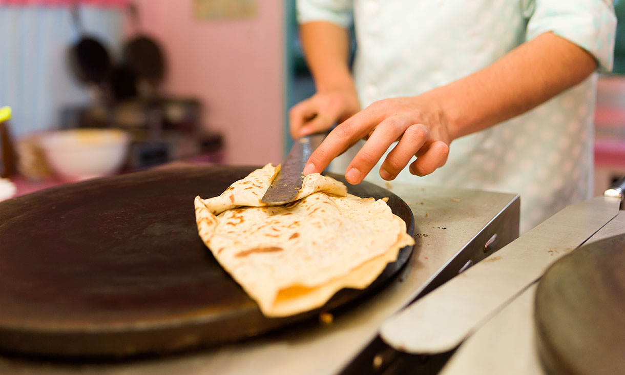 Young man cooking crepes with chocolate in a food truck.
