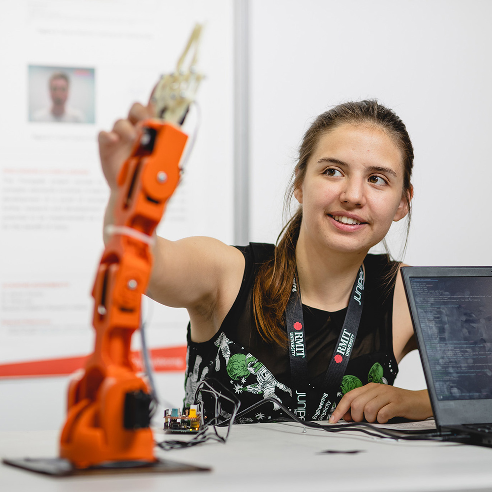 A young woman lifts a robotic arm, demonstrating innovation and her interest in robotics.