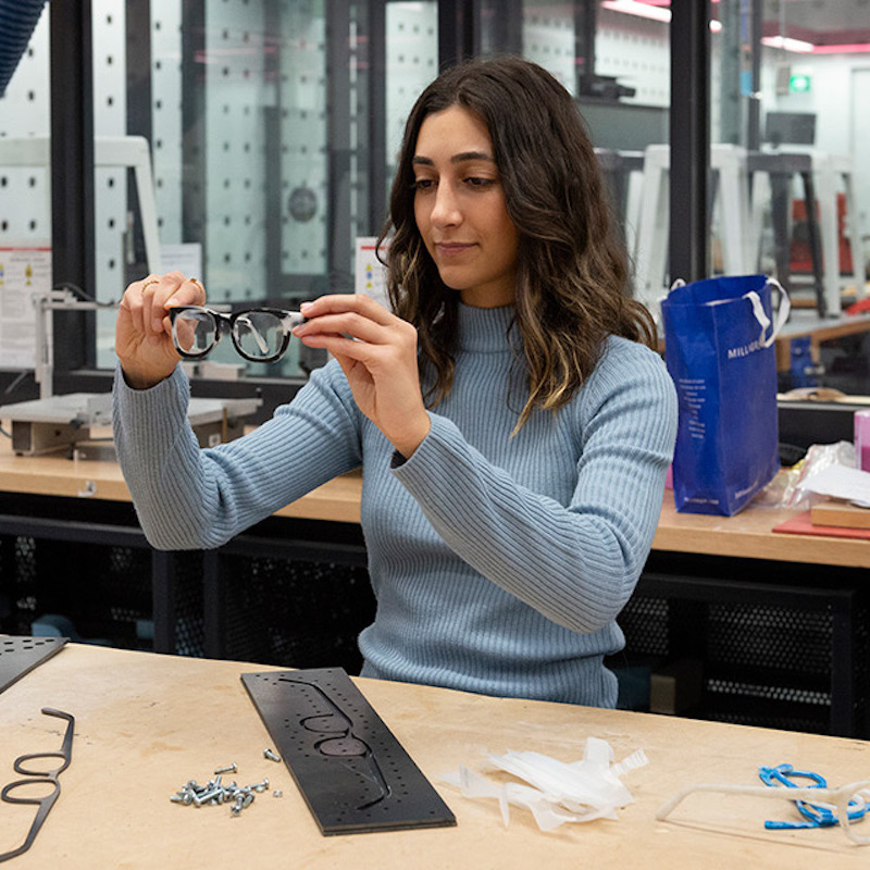 A woman holding up a pair of glasses with equipment in front of her