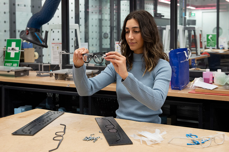 A woman holding up a pair of glasses with equipment in front of her