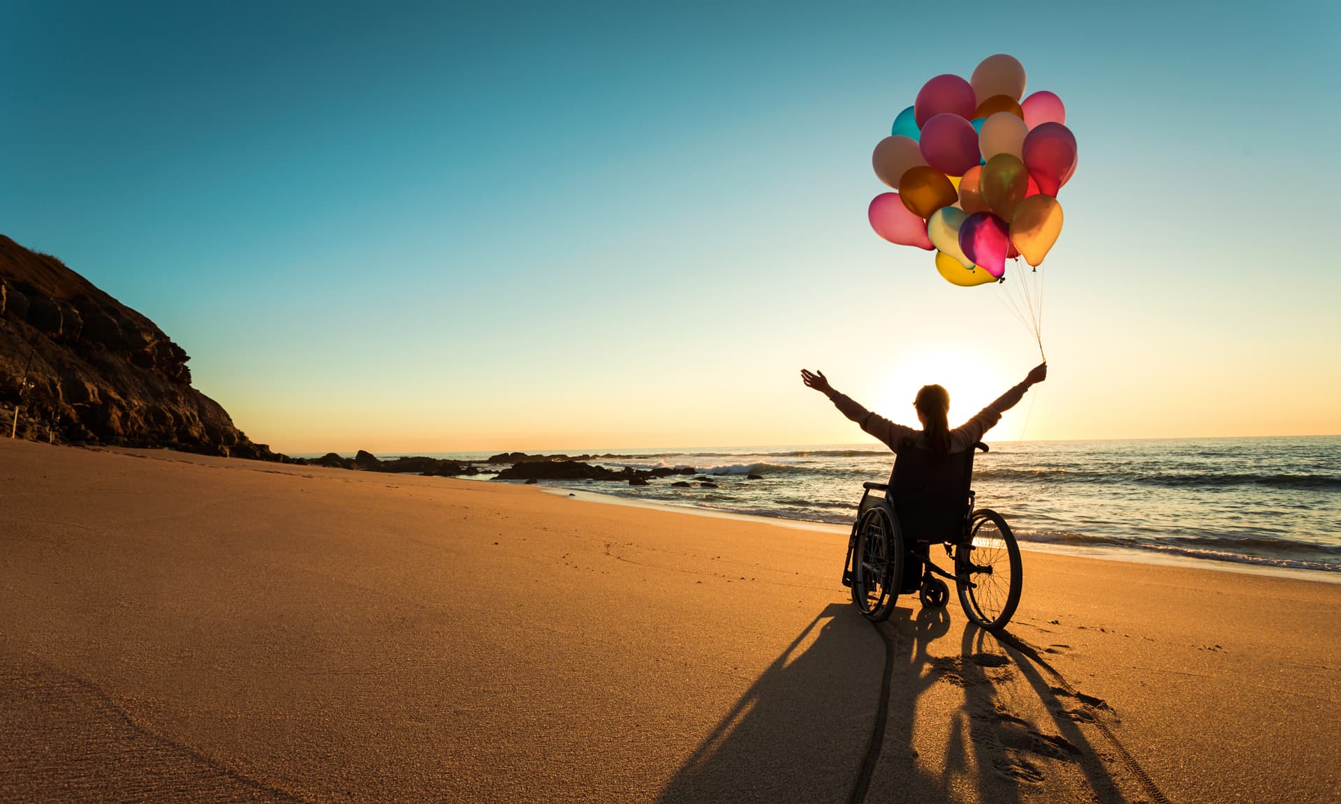 Person in wheelchair holding baloons on beach