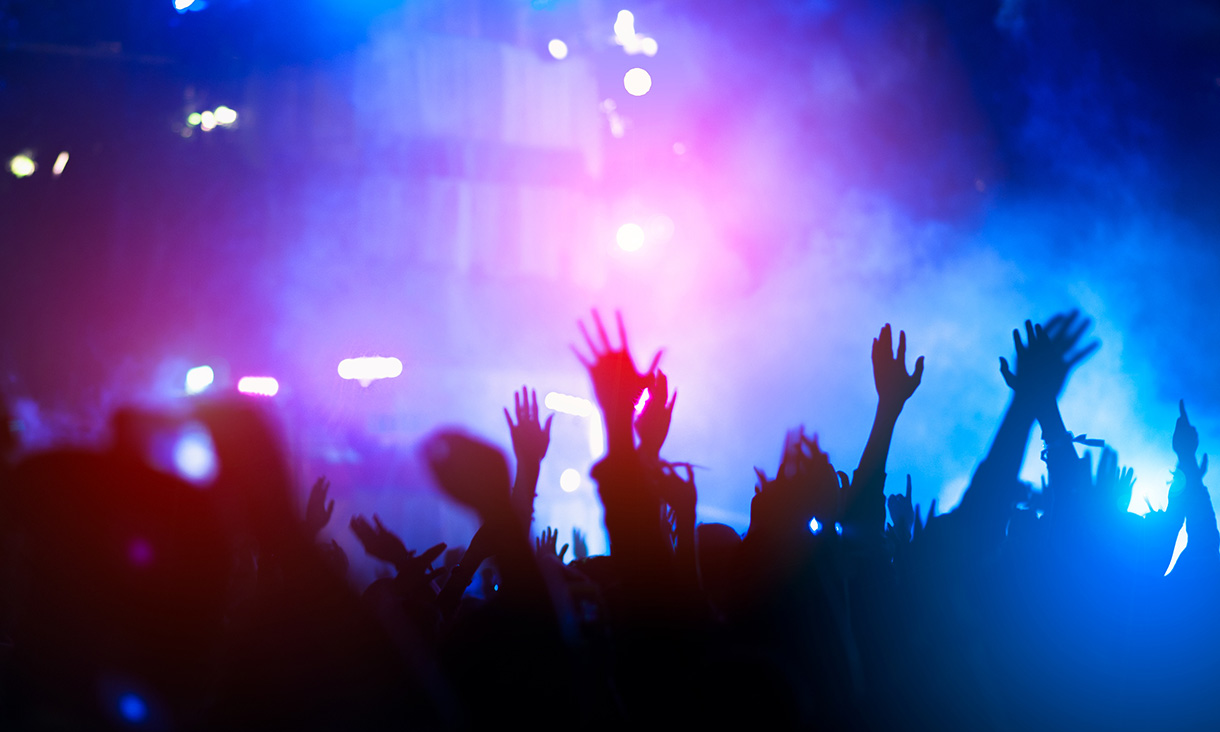 Silhouetted concertgoers raise their hands in the air