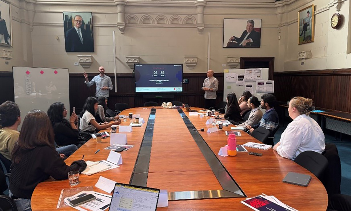 People sitting around a table with two people giving a presentation at the front