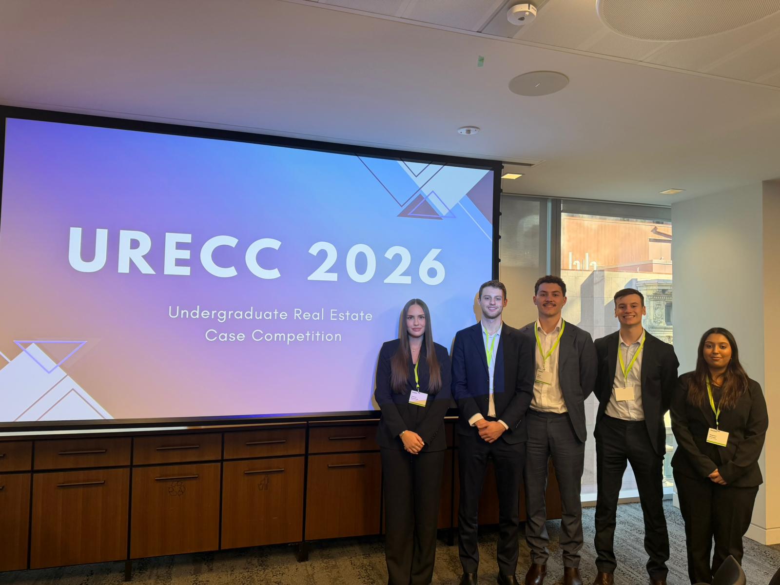 Group of people in business attire in front of presentation screen with the words URECC 2026