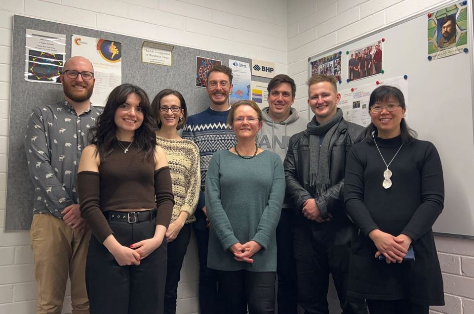 Eight people of mixed gender standing side by side smiling at the camera