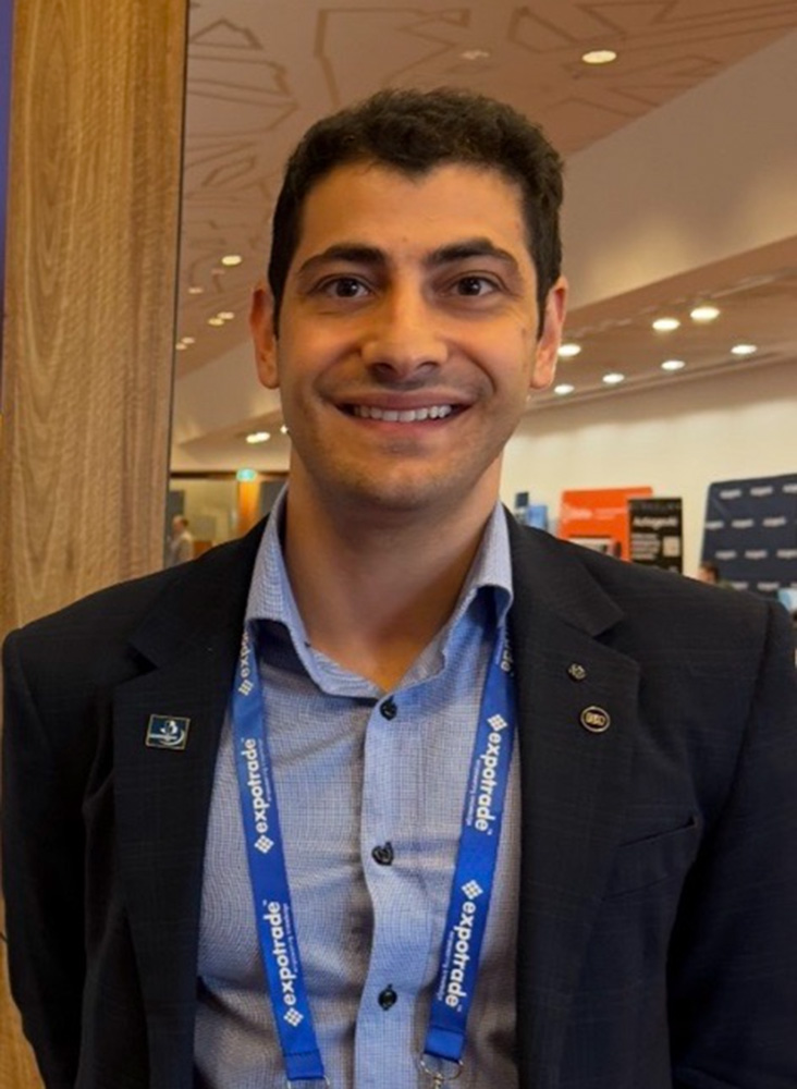 Andrea is at a conference wearing a suit and a blue lanyard.