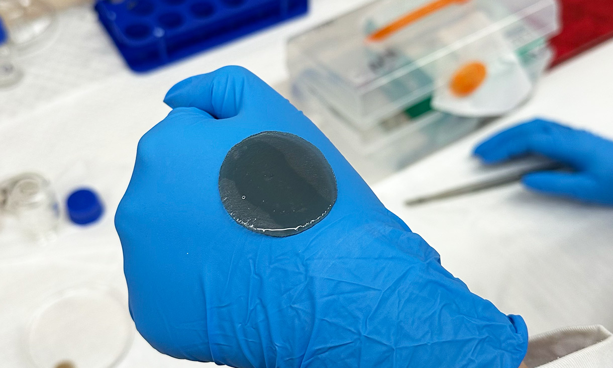 A person's hand is covered by a blue medical glove. On top of their hand is a liequid substance.