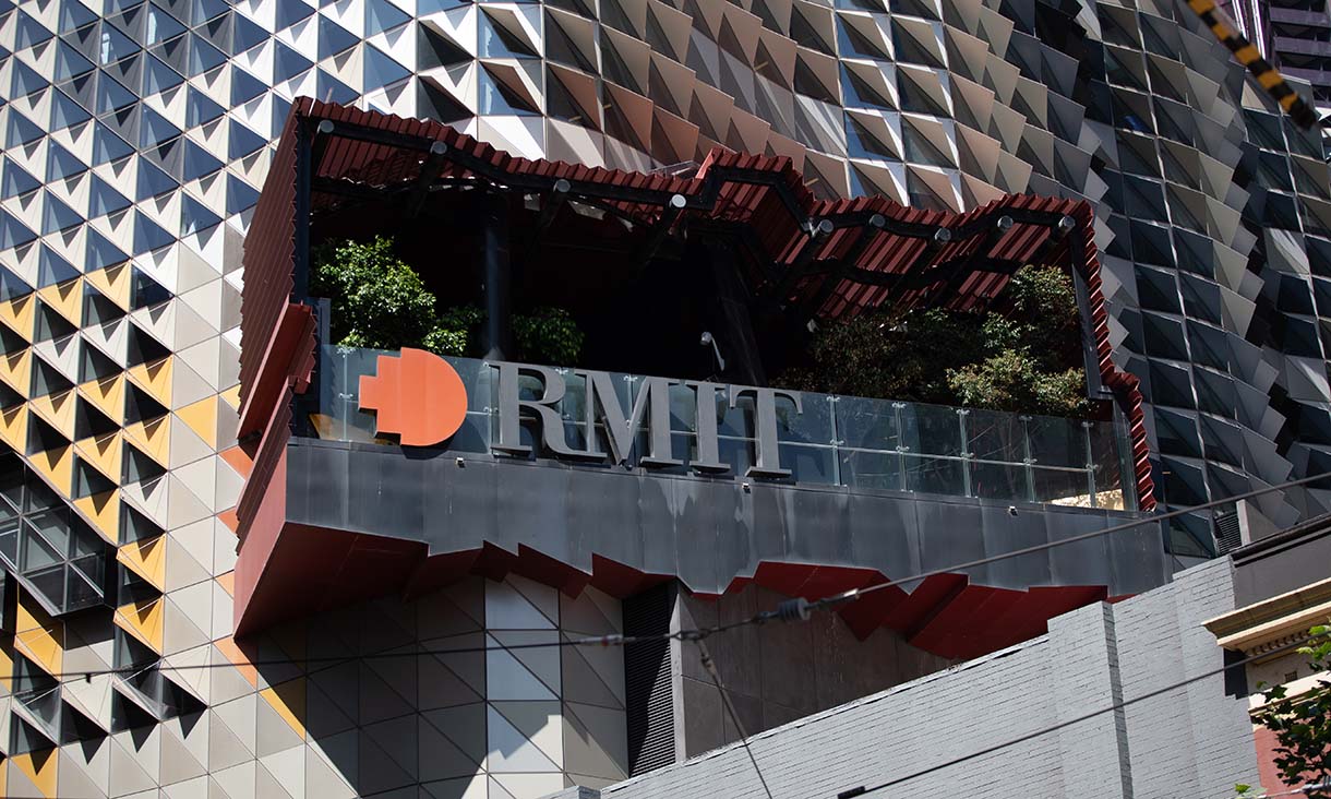 Exterior view of a modern RMIT University building, featuring a geometric patterned façade and a balcony with greenery, with a large RMIT logo displayed on a dark overhanging structure.