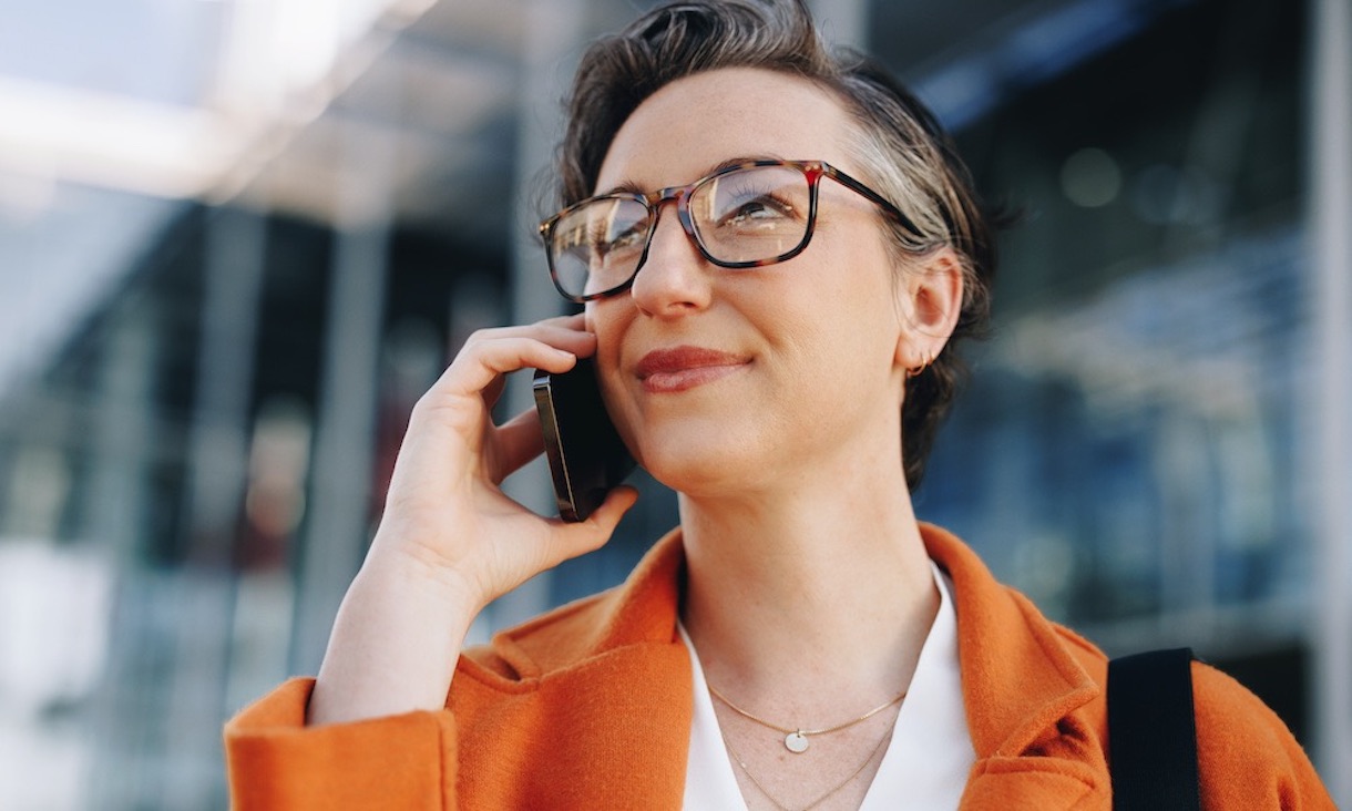 photo of a woman in business attire standing outside an office building and talking on a phone