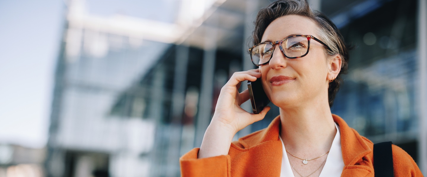 photo of a woman in business attire standing outside an office building and talking on a phone