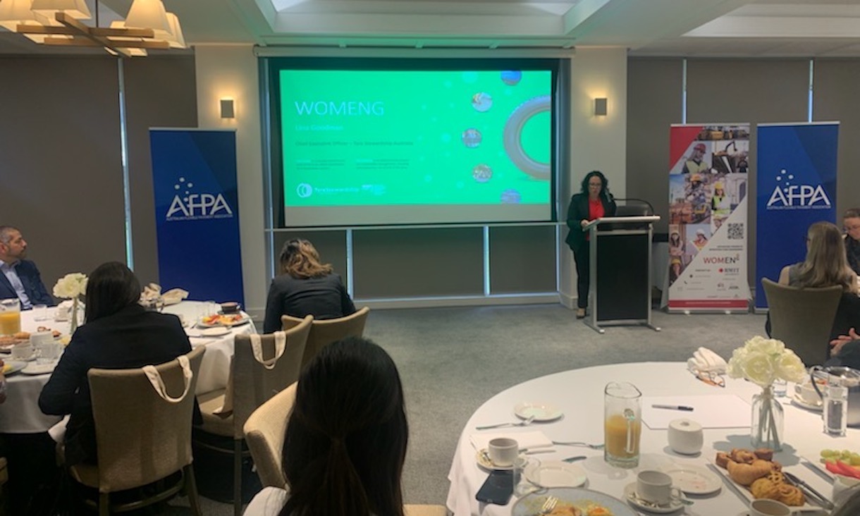 speaker at the WOMENG breakfast presenting in front of a projection of slides for the event