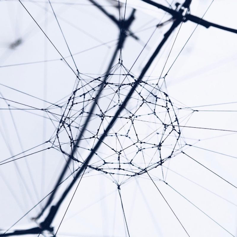 A geometric structure created from intersecting thin wires forming a web-like shape against a pale background.
