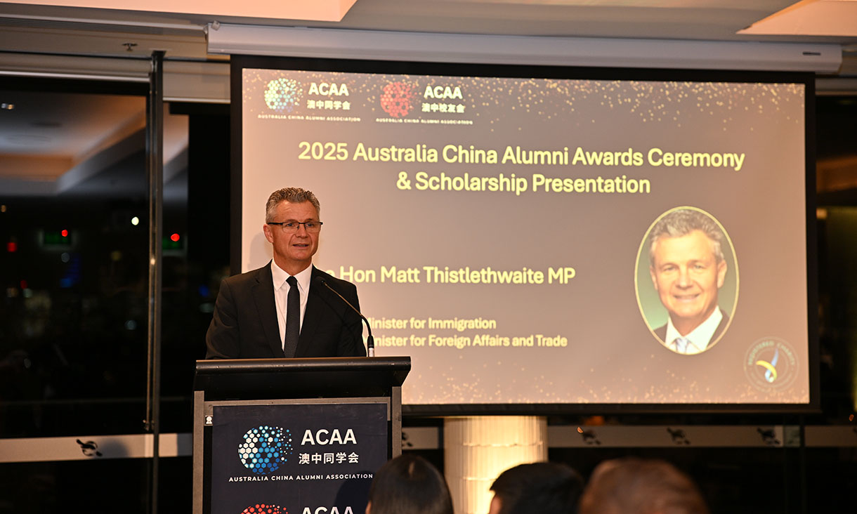 A man in a suit speaks at a podium during the 2025 Australia China Alumni Awards Ceremony & Scholarship Presentation.