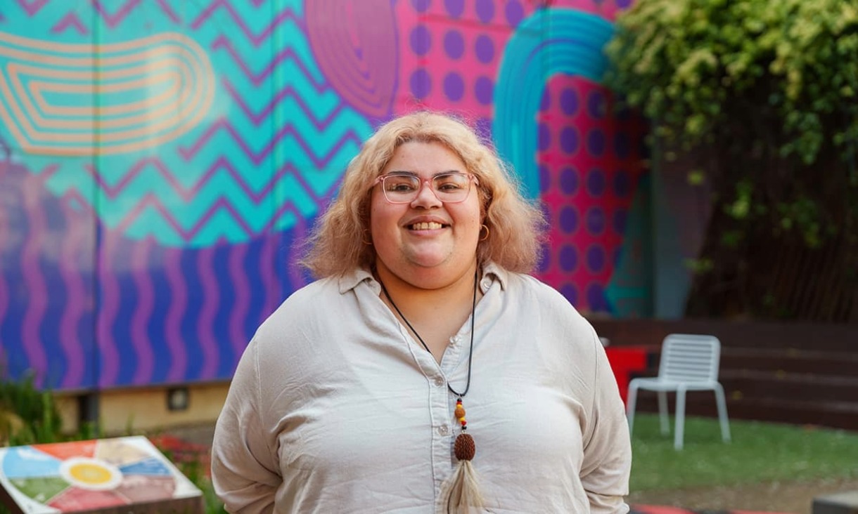 Portrait of woman smiling for a photo in front of an indigenous building.