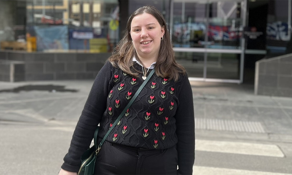 Isabelle is wearing a black dress and is standing to the right of Professor Cameron who is wearing a grey suit, white shirt and yellow patterned tie.