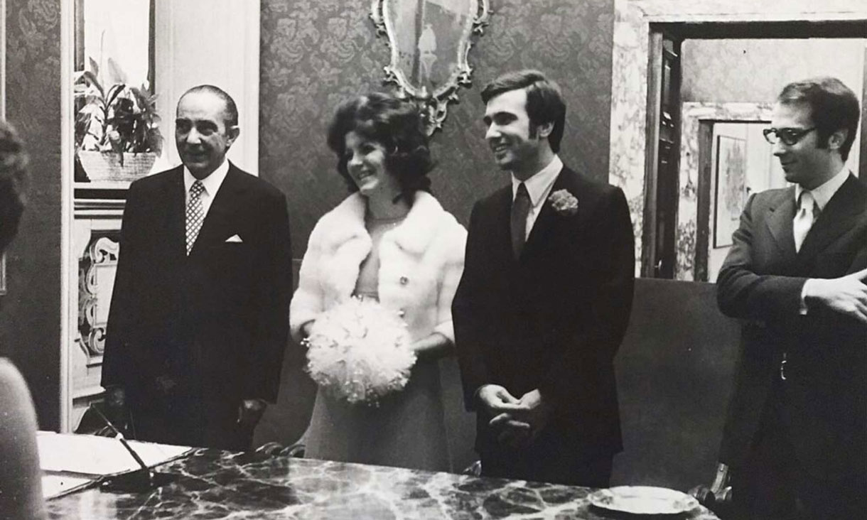 A black and white photo of Annemarie and Arturo getting married. They are standing together smiling with a man on each side. Their clothing and hair are in 1970s style.