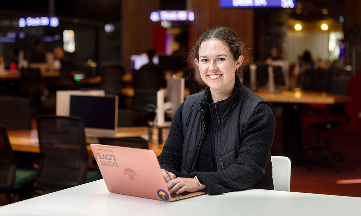 A girl at her laptop smiling at the camera.