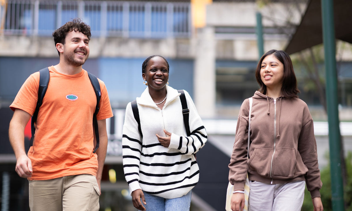 One male and two female students walk through campus smiling as if they are having a fun conversation.
