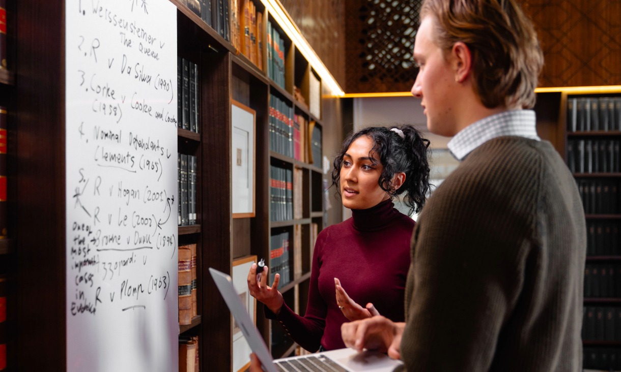 Two people working together looking at a whiteboard.