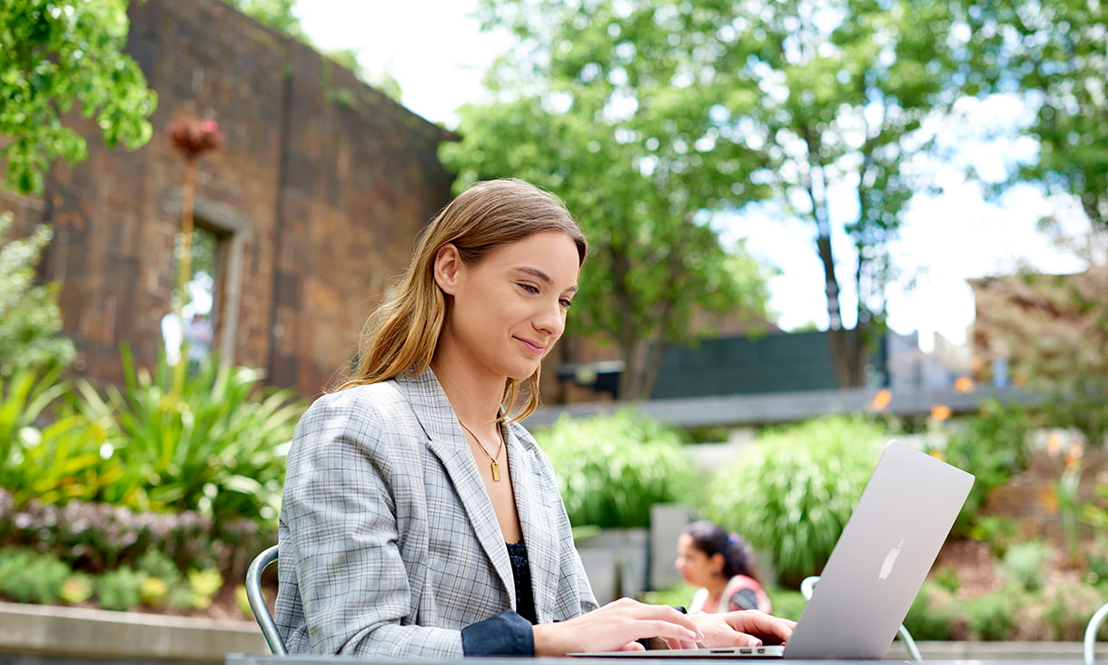 Communications student Keira studying on laptop while outdoors, on campus