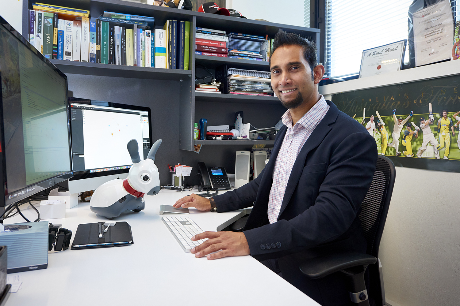 John Thangarajah sitting at his desk with his robot dog