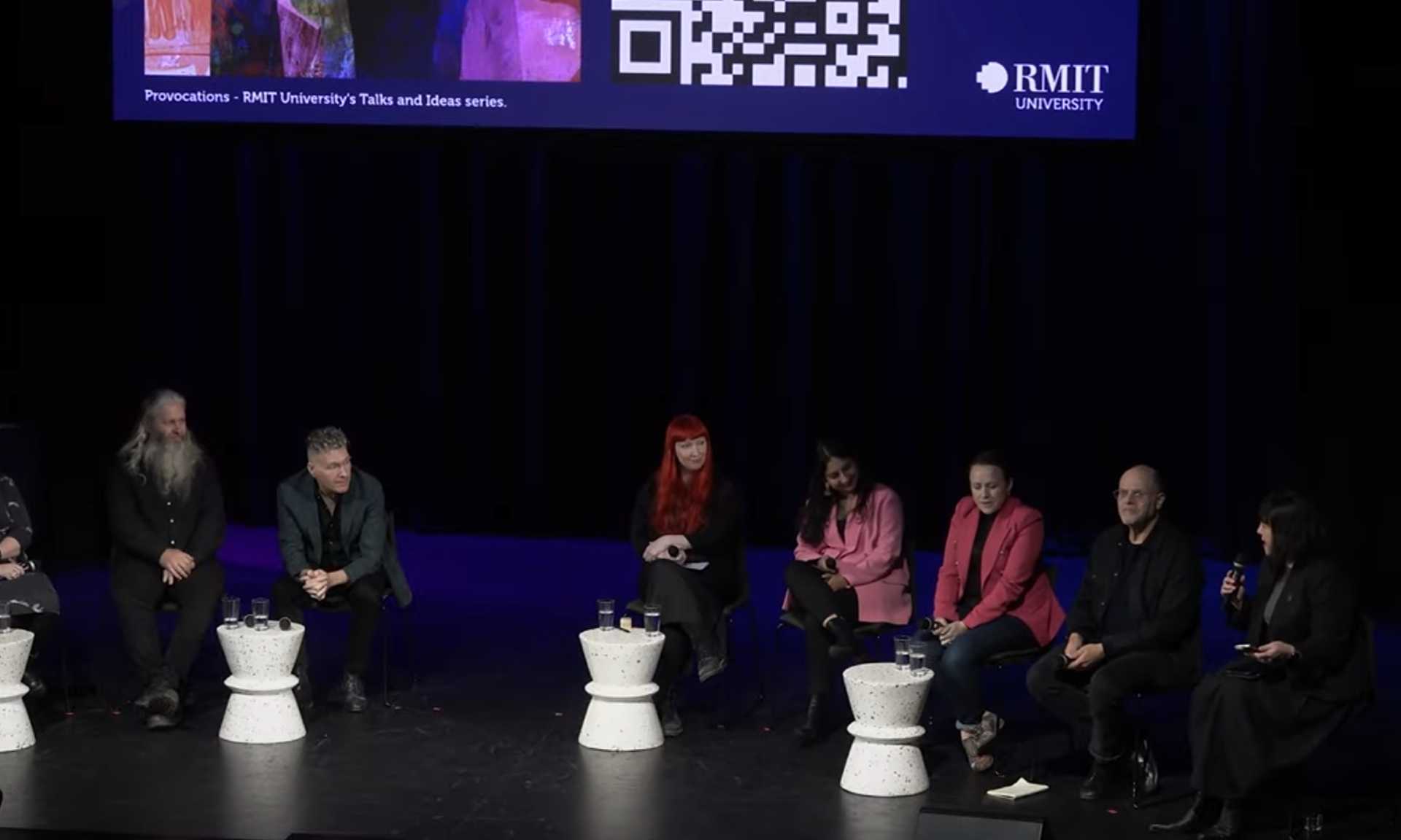 Panel discussion featuring several speakers seated on a dark stage, with an RMIT University “Provocations” Talks and Ideas Series banner displayed above them.