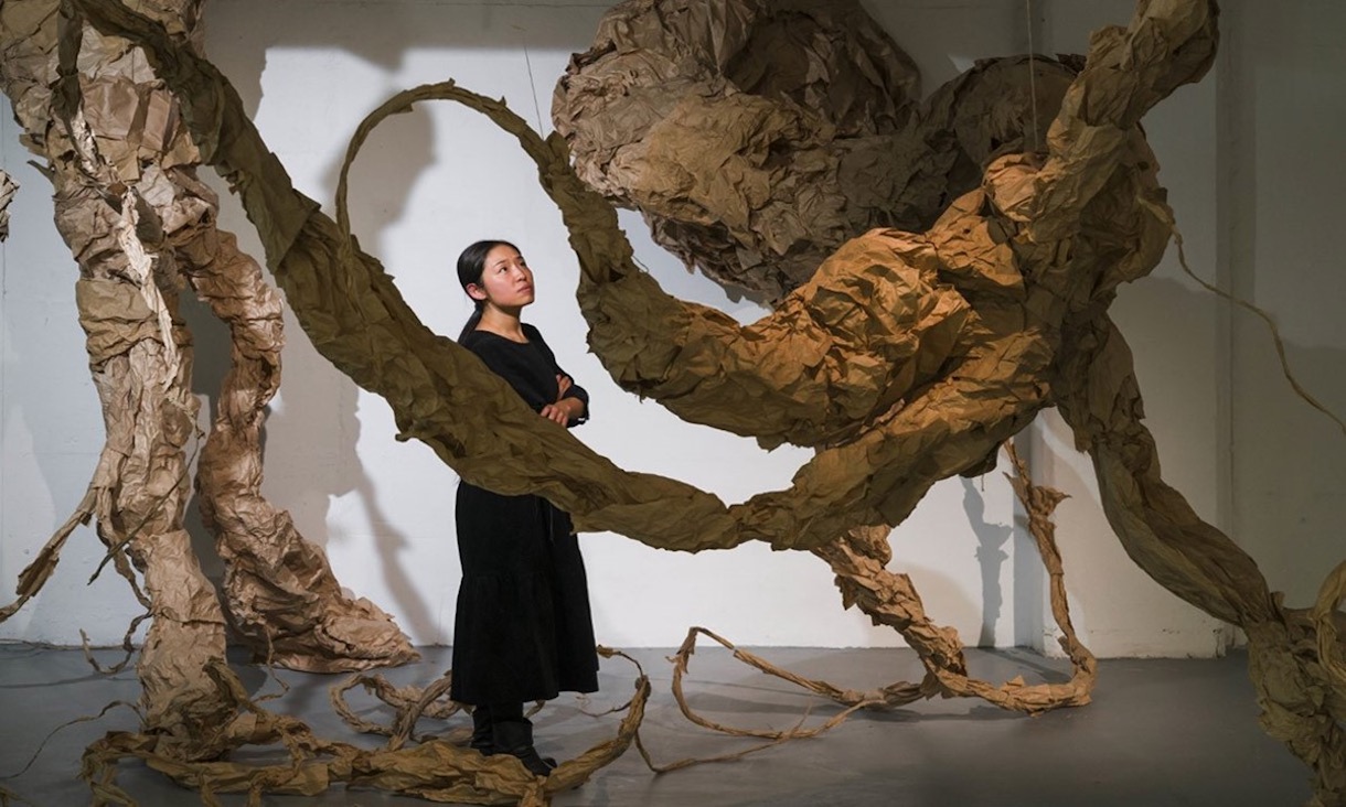 a woman visiting an art exhibit which is a room full of large scale sinuous forms made out of paper