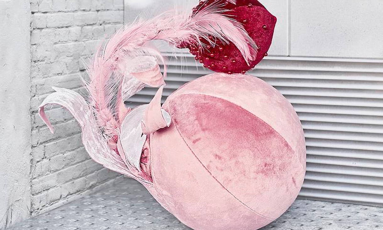 organic looking textile artwork, a pink velour sphere with feathers and a red bulb coming out of it