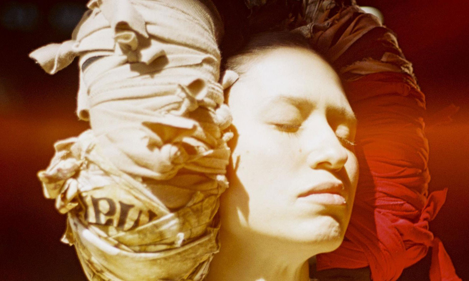 Close up of person's face with eyes closed and bandaged objects around their head