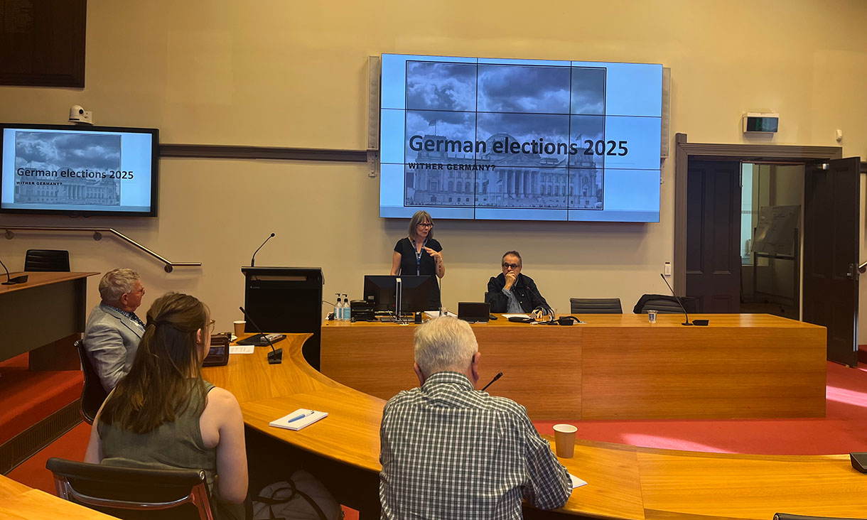 A group of people attending a seminar in a lecture room with a large screen displaying "German elections 2025"